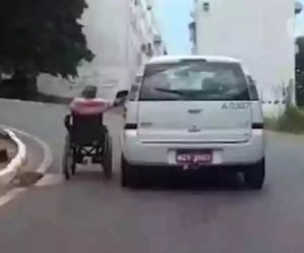 Man in wheelchair hitches a ride by clinging to car